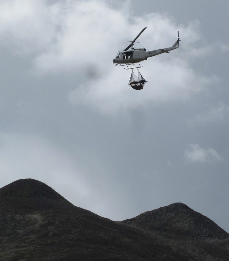 AirCam helicopter flying an external load over mountain terrain